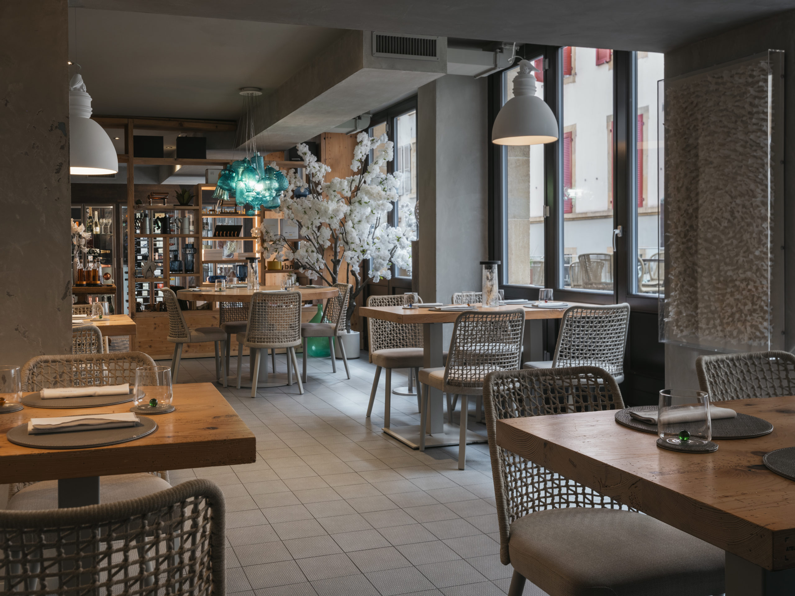 Salle du restaurant gastronomique La Dispensa à Neuchâtel, ambiance élégante et conviviale avec mobilier en bois naturel, luminaires design et lumière douce méditerranéenne.