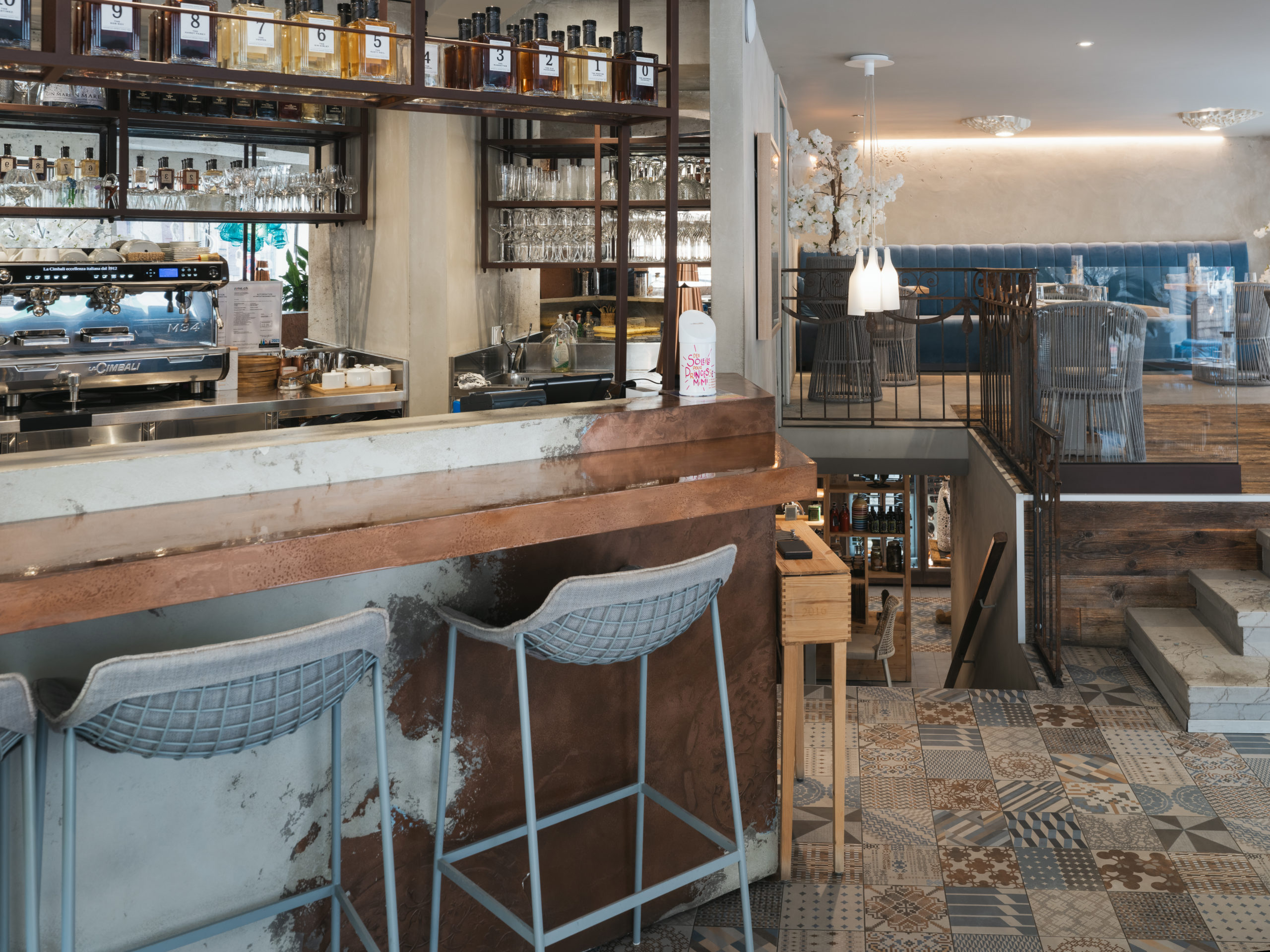 Bar du restaurant gastronomique La Dispensa à Neuchâtel, comptoir en cuivre, chaises design, étagères de spiritueux italiens et ambiance contemporaine chaleureuse.